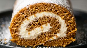 Ultra close-up macro food photography of a slice of classic spiced pumpkin roll with luscious cream cheese filling and powdered sugar